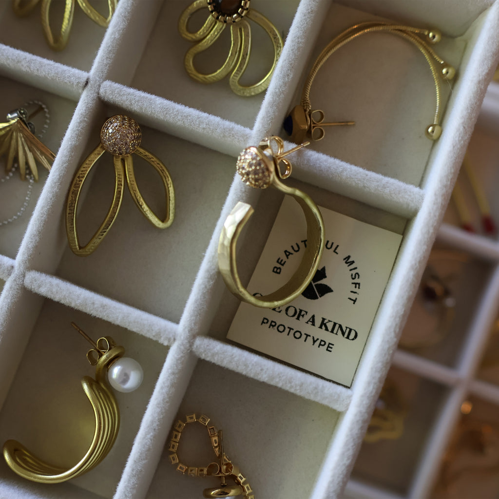 Gold earrings displayed in a jewelry box with 'Beautiful Misfit' label.