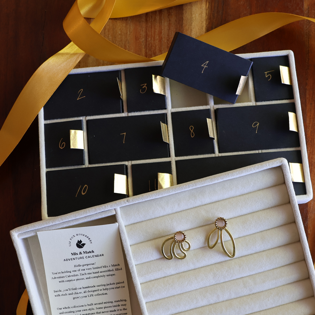 Advent calendar with gold earrings and a yellow ribbon on a wooden surface